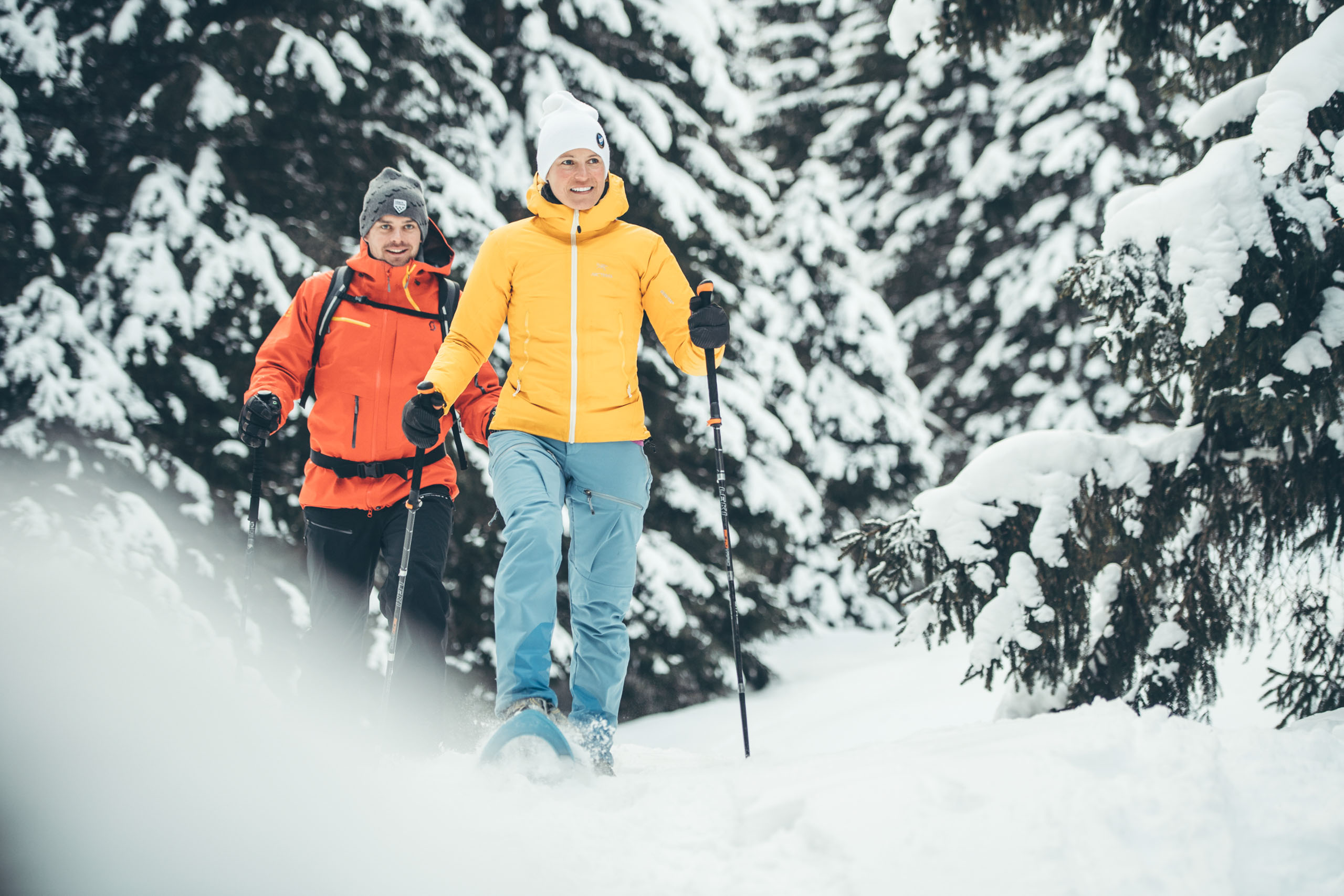 A man and a woman snowshoeing through a winter landscape